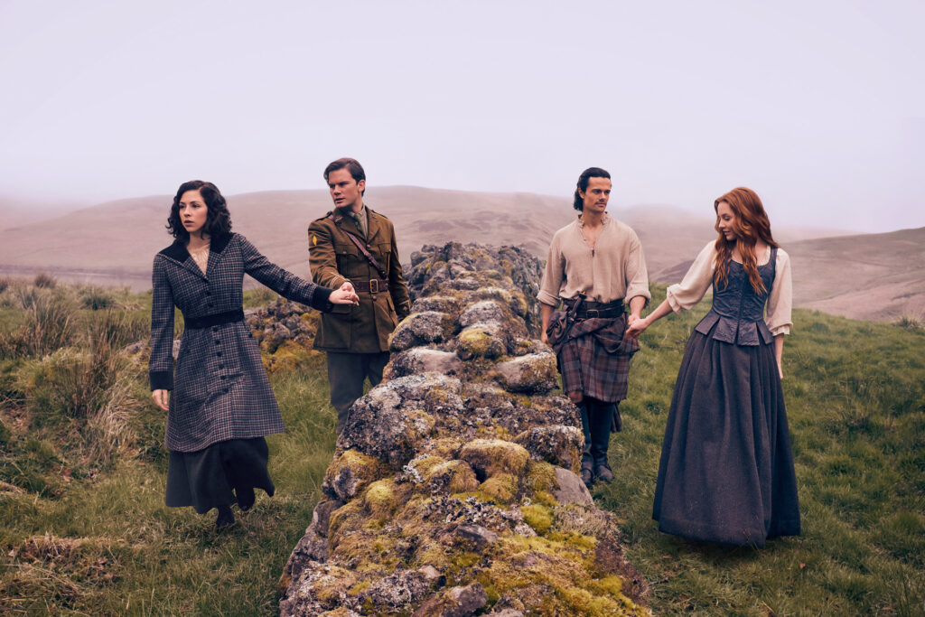 Los actores principales de Outlander Blood of my Blood tomados de las manos sobre un muro de piedra antigua en las Tierras Altas de Escocia