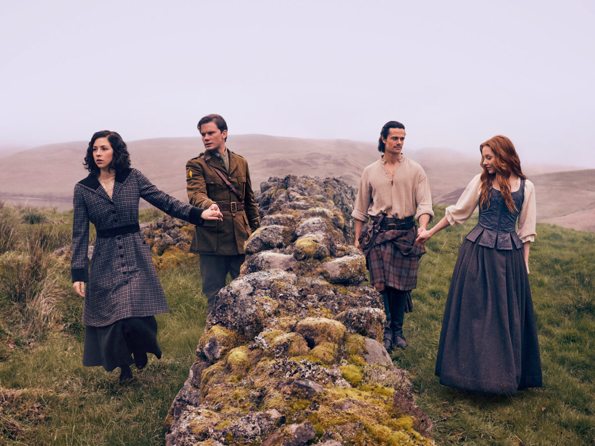 Los actores principales de Outlander Blood of my Blood tomados de las manos sobre un muro de piedra antigua en las Tierras Altas de Escocia