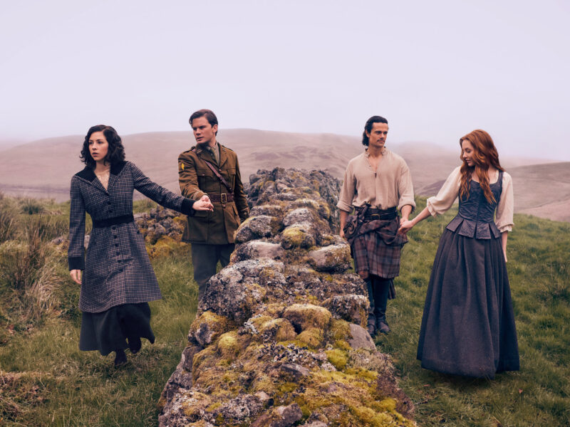 Los actores principales de Outlander Blood of my Blood tomados de las manos sobre un muro de piedra antigua en las Tierras Altas de Escocia